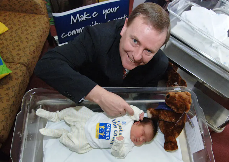 A man in a suit smiles above a sleeping newborn baby
