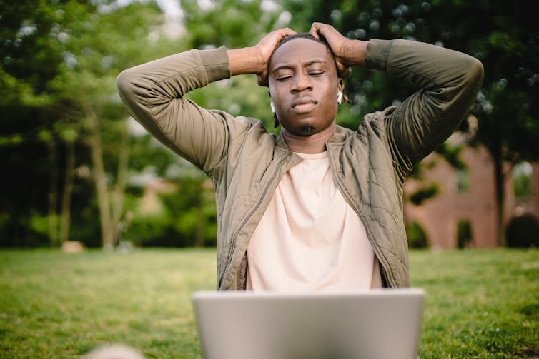 A young man sitting in a park using a laptop.