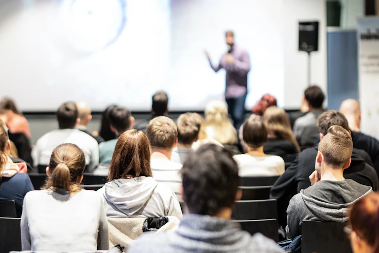 A group of young people sit in rows and listen to a speaker.