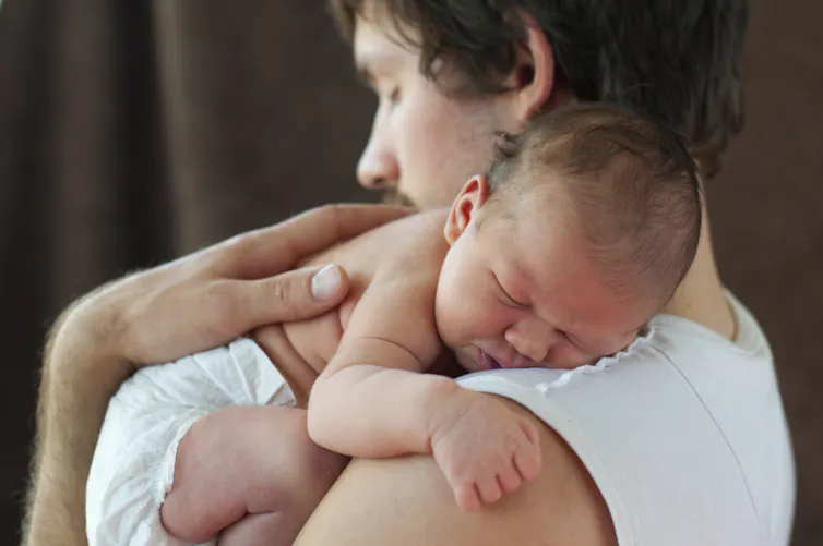 Dad holds a tiny newborn against his shoulder.