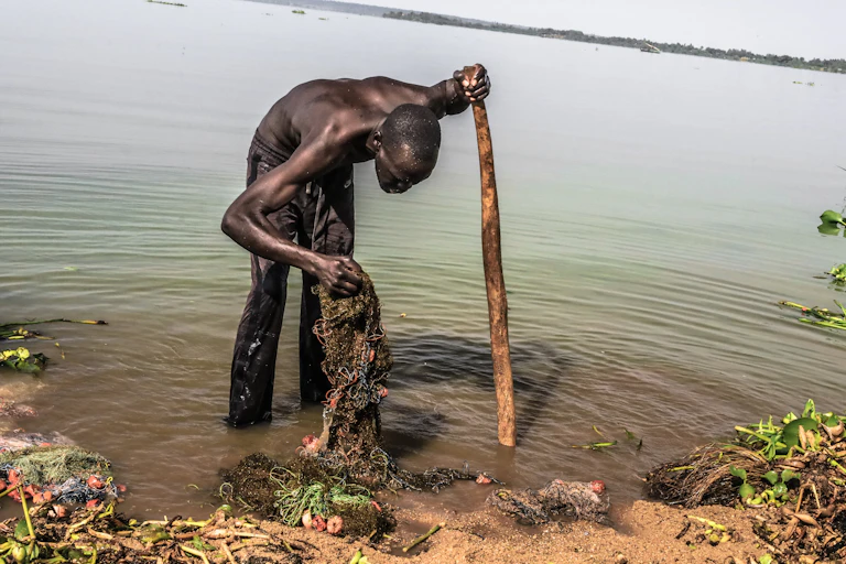 A man cleans his fishing net by the shores of a lake