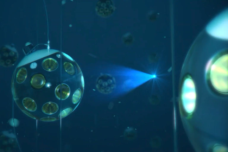 Image showing a a glowing blue dot travelling through a grid of spheres floating underwater