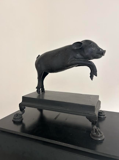 Escultura de un cerdito que salta en bronce negro.