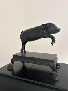 Escultura de un cerdito que salta en bronce negro.