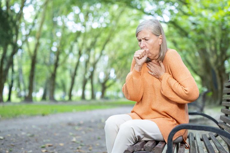 Woman sitting on a park bench, coughing.