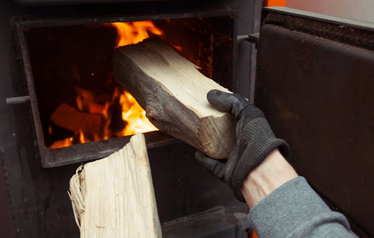 A person placing a piece of wood in a stove.