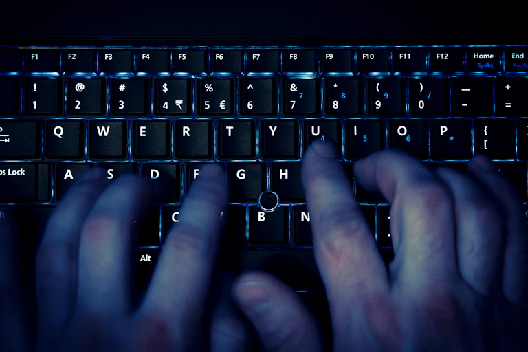 View from above of fingers typing on a keyboard in the dark
