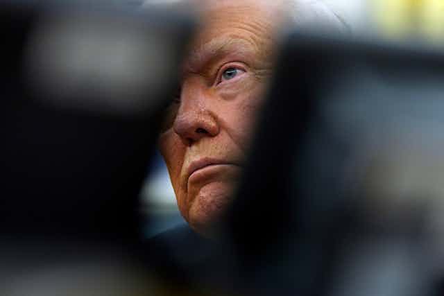 An elderly man's tanned face is partially obscured.