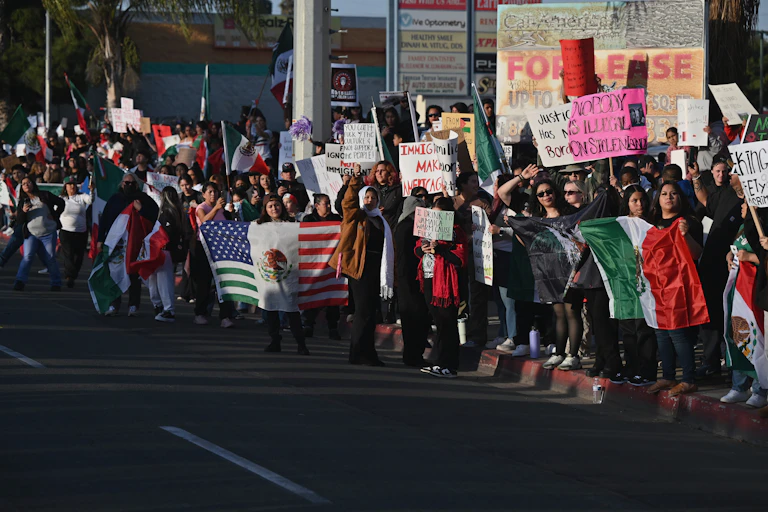 Large crowd of people waving American and Mexican flags and holding pro-immigration signs stand on a roadside