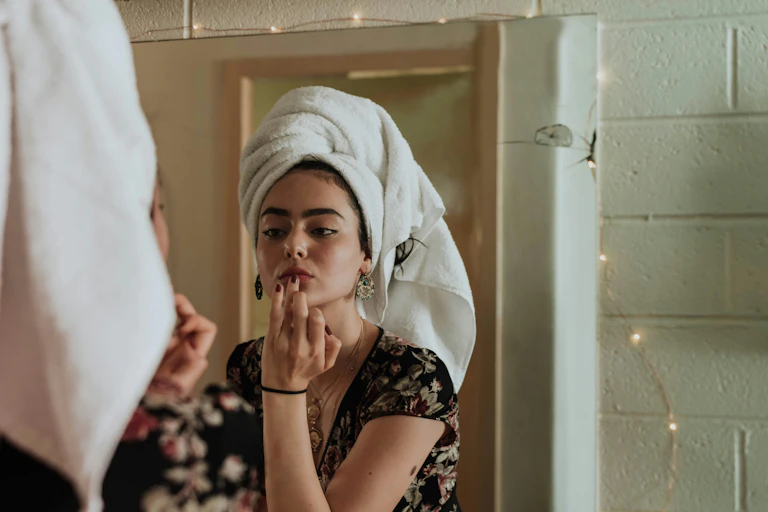 A woman puts makeup on her lips while looking in the mirror