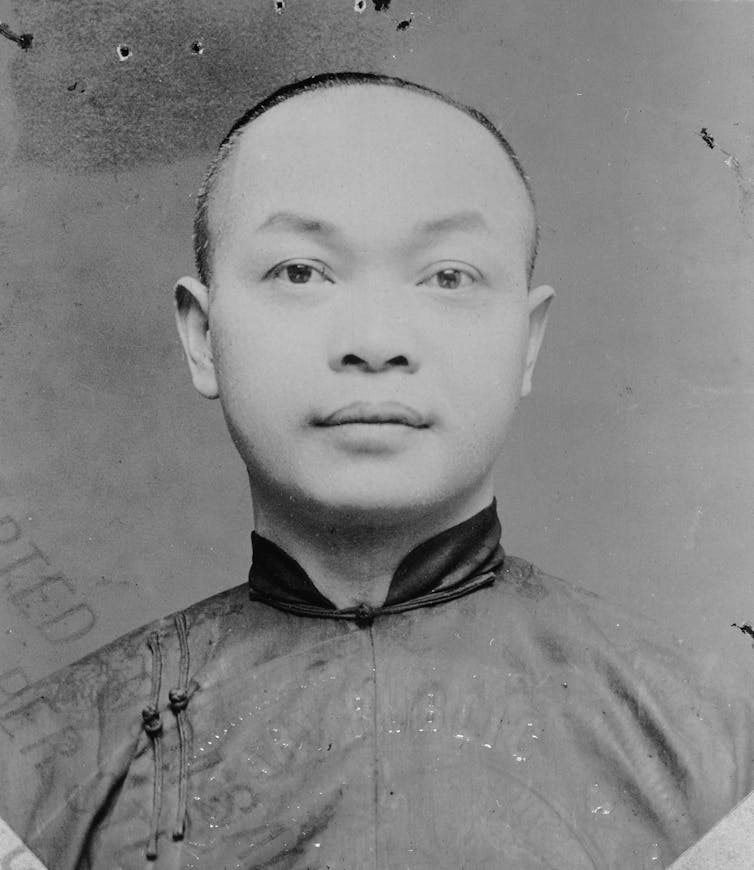 A black and white photo shows a Chinese man with very short hair looking at the camera.