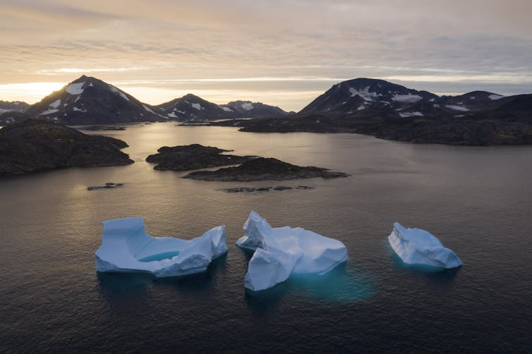 des icebergs flottent dans l’eau au lever du soleil avec des montagnes en arrière-plan