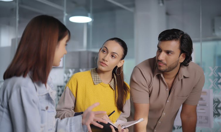 Un joven y una mujer joven escuchan atentamente a otra mujer que ha vuelto a la cámara