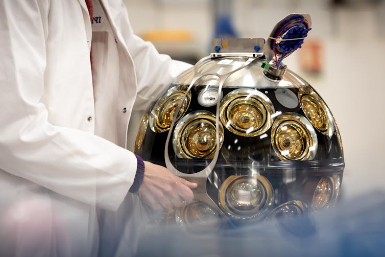 Photo of a person in a lab coat handling a large spherical object covered in lenses.