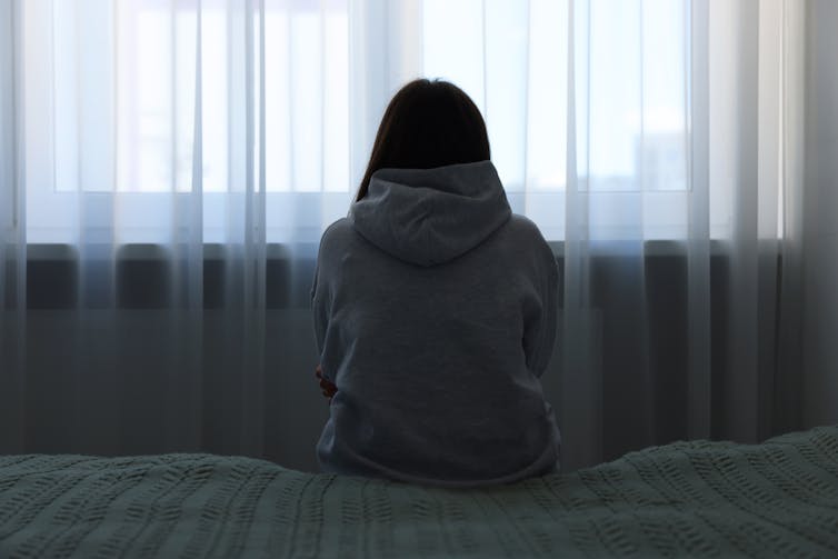 The woman sat on the slotted bed against the window.