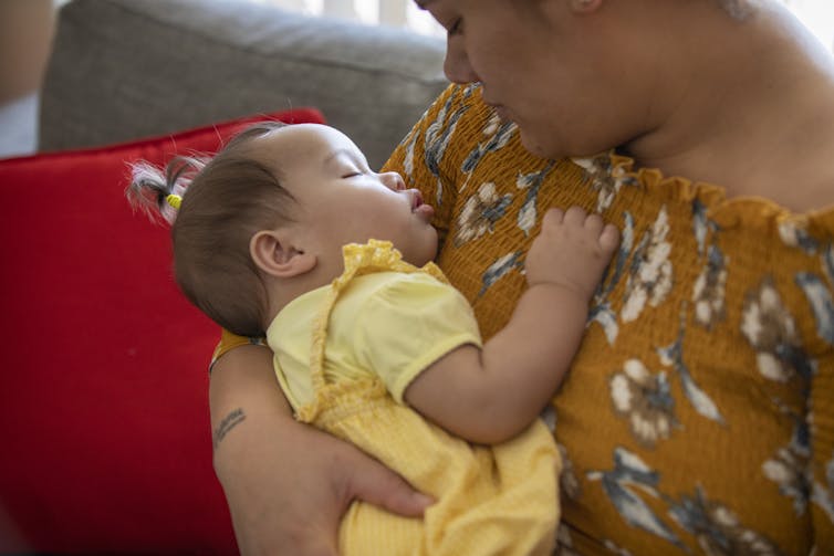 A woman holds a sleeping infant against her chest.