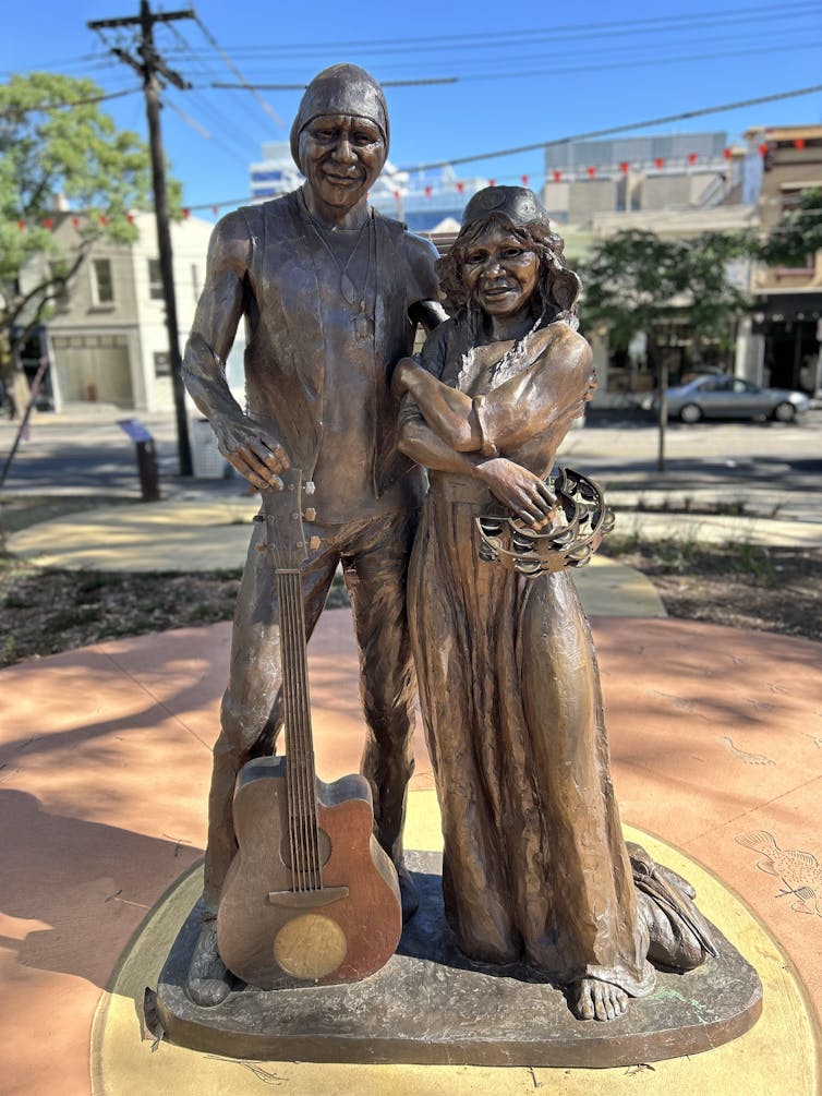 The full-length statue. Archie's hand rests on a guitar; Ruby holds a tambourine.