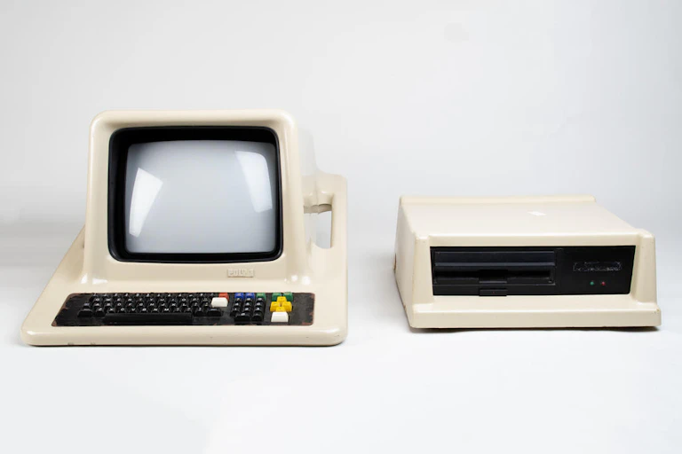 The computer and keyboard are enclosed in a cream coloured moulded plastic. There is a standard computer keyboard, black in colour with black keys and white characters on the tabs.