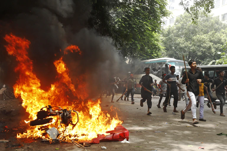 Protestors carrying sticks run past a motorcycle on fire.