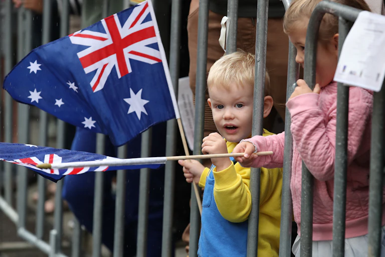 A small blond boy waving an Australian flag behind a crowd barrier