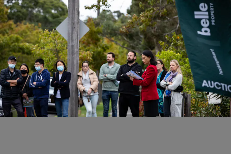 Several people standing on a street outside a house auction