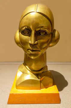 A brass sculpture of a woman's head, looking stark and almost robotic.