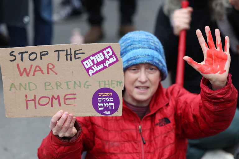 An Israeli peace protester in Jerusalem holds up a hand painted red and a placard calling for peace and the return of the hostages.