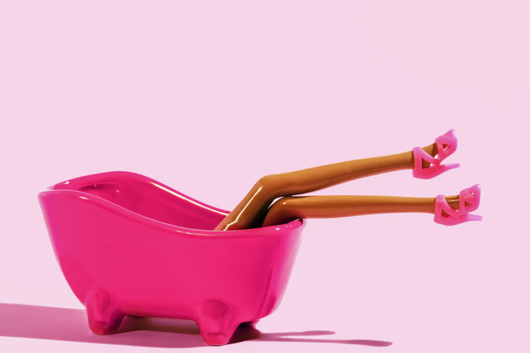 une baignoire en plastique rose d'où dépassent deux très longues jambes de poupée caractérisitques de Barbie avec des talons aiguilles roses