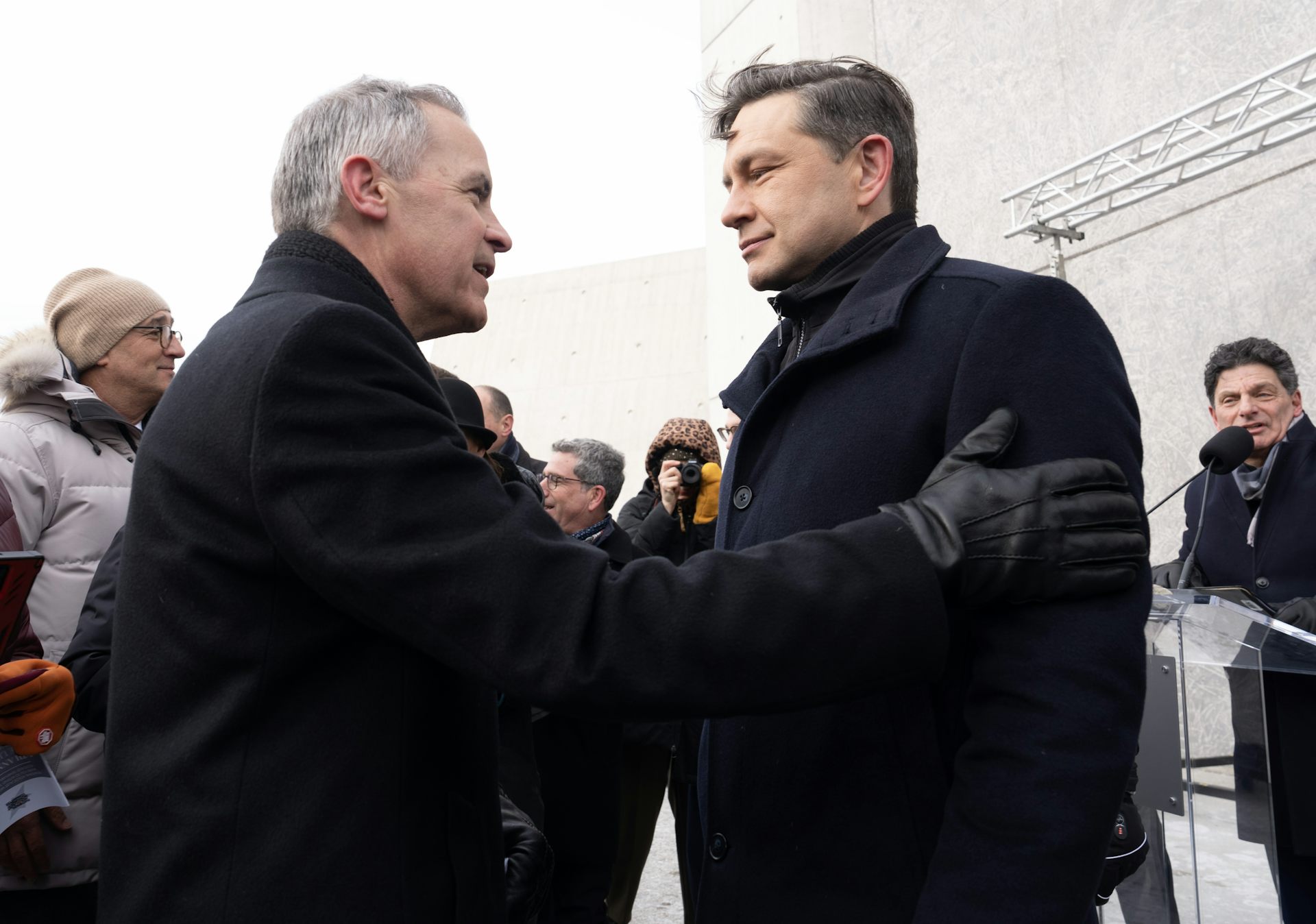 Un homme aux cheveux gris et vêtu d'un manteau d'hiver noir pose sa main sur le bras d'un homme aux cheveux noirs et vêtu d'un manteau noir