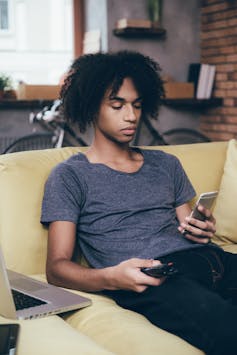 A teen holding remote control with a phone