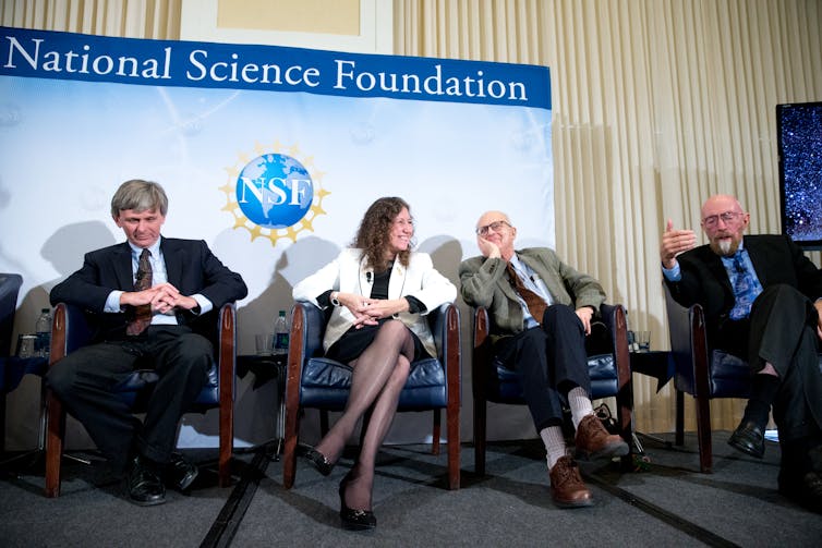 Four scientists sitting in front of a sign reading National Science Foundation, with the NSF logo