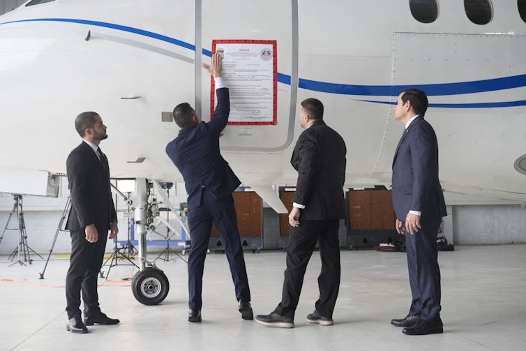 Four men in suits attach a sign on an airplane.