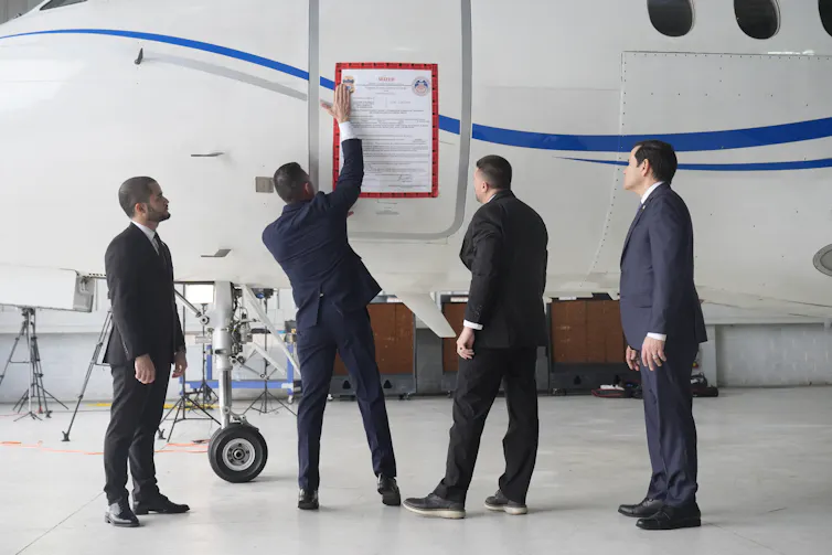 Four men in suits attach a sign on an airplane.