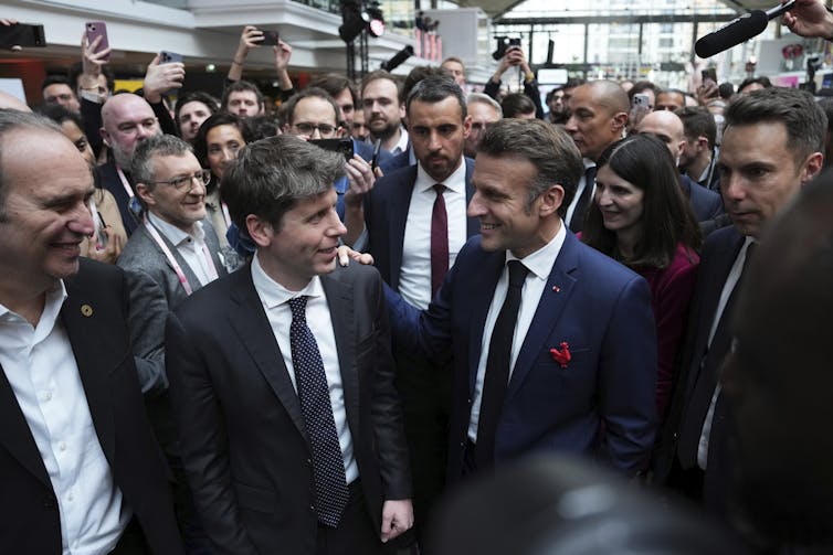 two men in suits stand among a crowd
