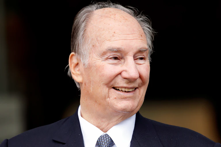 A gray-haired man, dressed in a blue suit and tie, looking ahead and smiling.