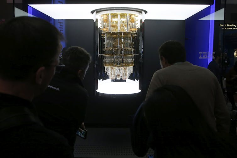 A crowd looks at a quantum computer on display, which looks like a large structure containing wires and electronics.