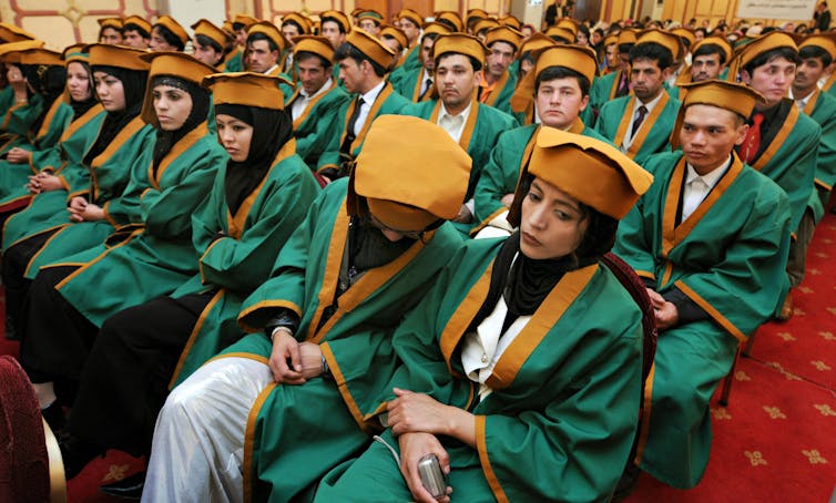 Young women and men in green graduation robes and caps seated in several rows in a large hall.