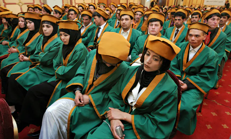 Young women and men in green graduation robes and caps seated in several rows in a large hall.