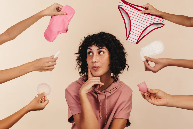 woman looking at arms surrounding her, all holding different red and white reusable period products
