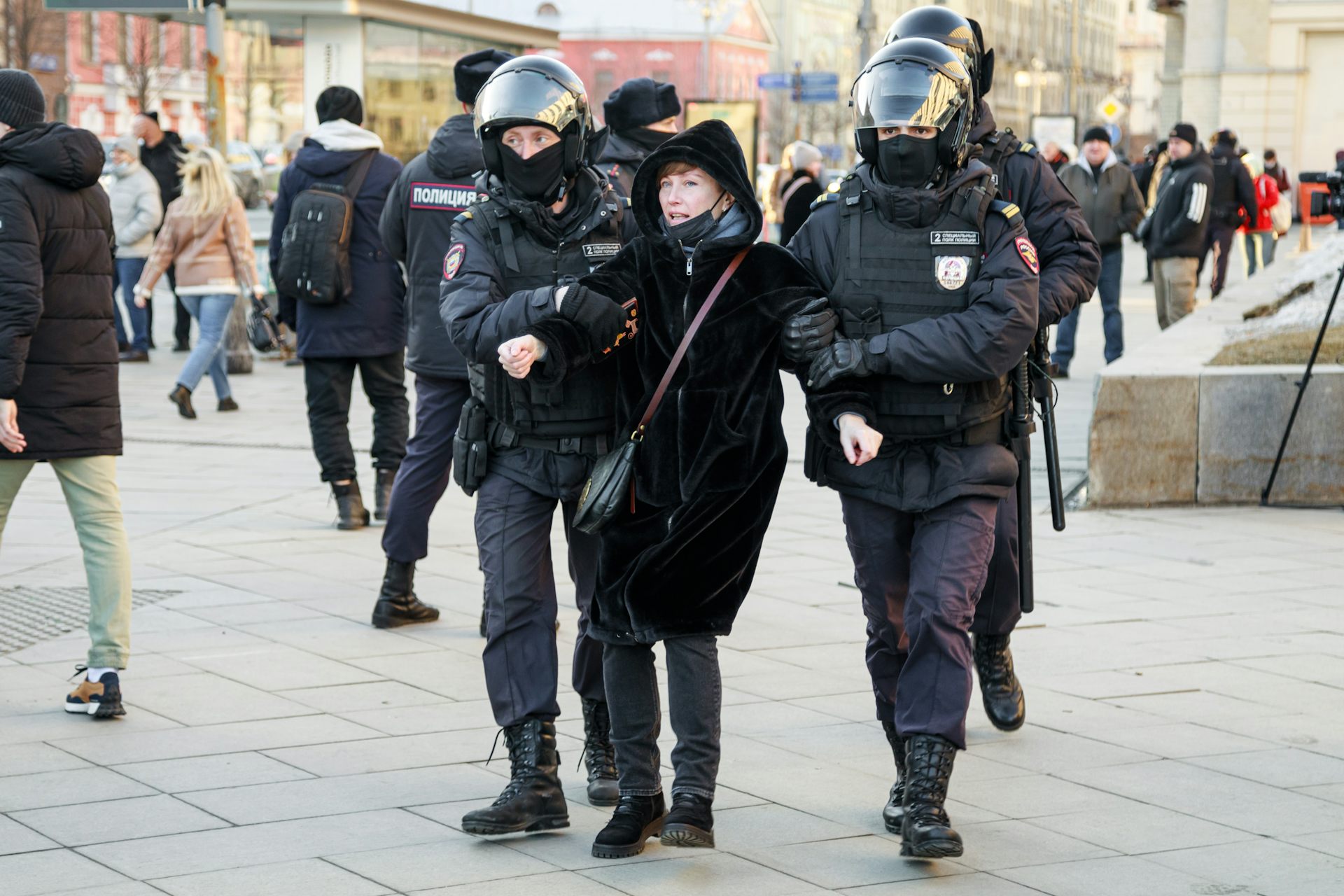 A female anti-war protester is held by two police in riot gear.