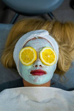 A blonde woman lies with a green face mask and two orange slices over her eyes