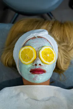 A blonde woman lies with a green face mask and two orange slices over her eyes