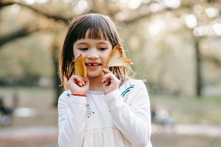 A young girl holds leaves to her face.