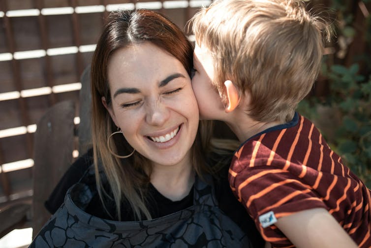 A woman smiles as a young boy gives her a kiss.