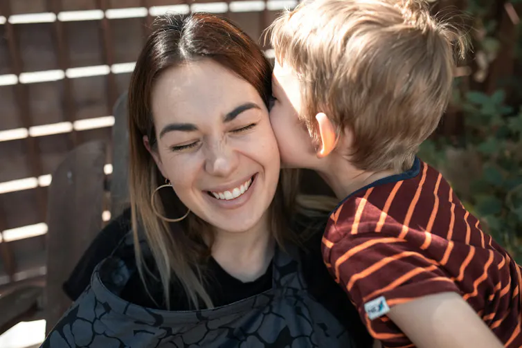 A woman smiles as a young boy gives her a kiss.