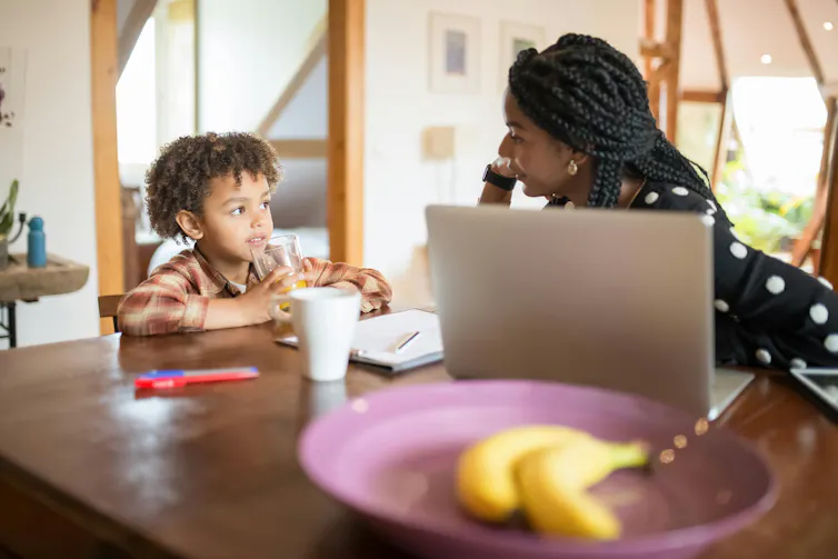 A woman and young boy talk at a table. The boy is drinking, the woman has a laptop in front of her.