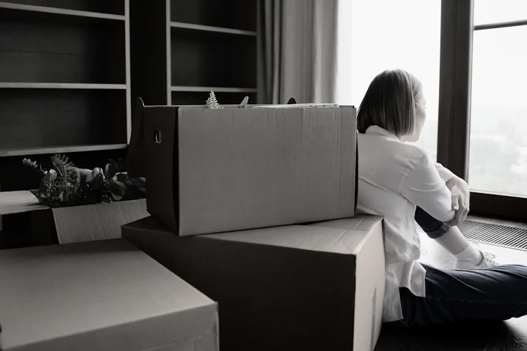 Black-and-white photo of woman sitting on the floor with packing boxes
