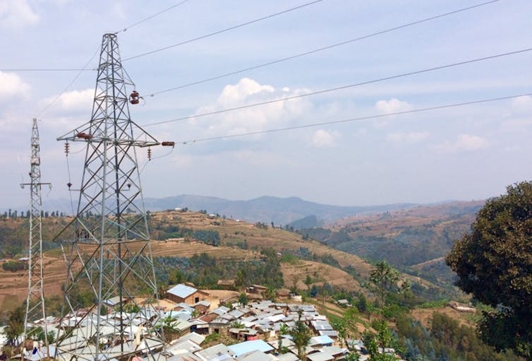 view over shacks with solar panels on roofs, pylon in foreground