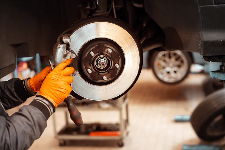 hands of mechanic in orange glove fixing brake pads on wheel of car