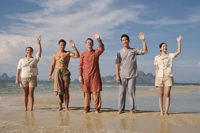 Staff at the White Lotus Thaliand waving on a beach.